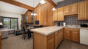 A kitchen with wooden cabinets, a large island, a stone fireplace, and a dining area with a sofa and chairs.
