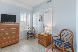 A room with a television on a wooden cabinet, two wicker chairs, a small wooden dresser, and a door with a sign. - ☀️Casablanca: Oceanfront Home w/ Ocean Views☀️ (Kure Beach)