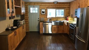 Eine holzgetäfelte Küche im Chalet-Stil mit einem Edelstahl-Kühlschrank, einem Geschirrspüler und einem Spülbecken.