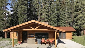 Ein Blockhaus mit überdachter Veranda, Garage und einer Terrassenfläche mit Sitzgelegenheiten.