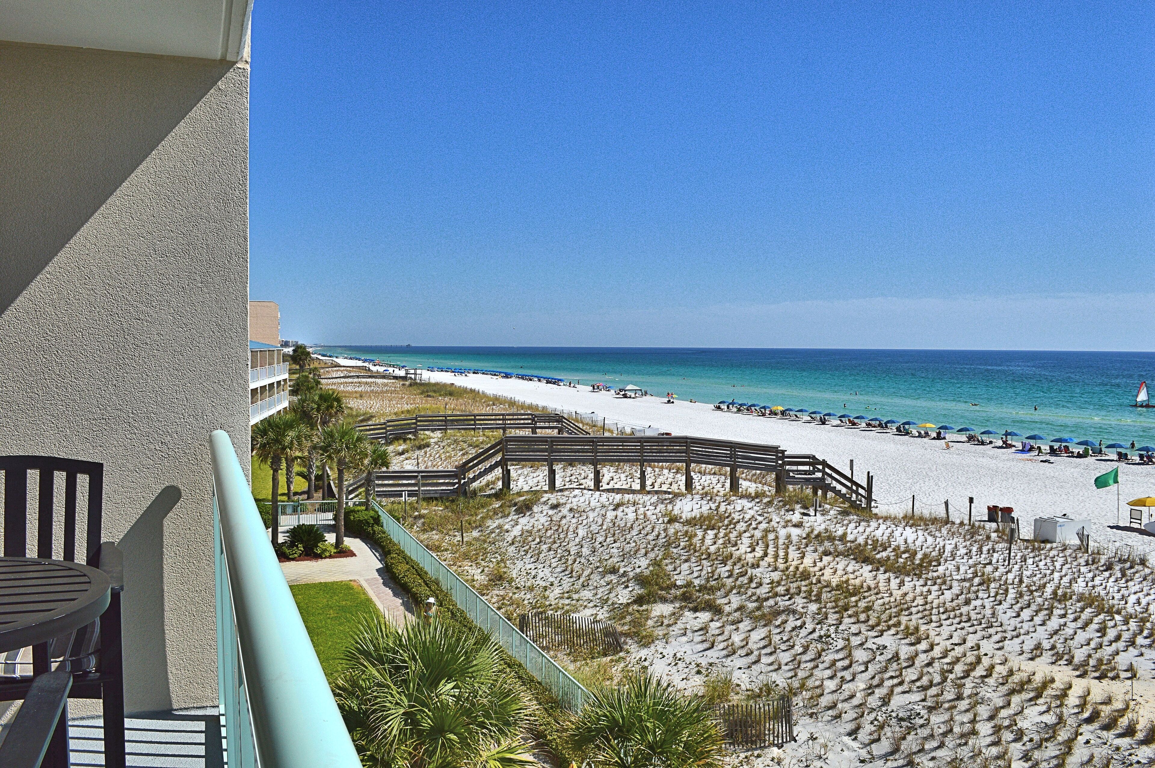 A beach view from a balcony with a wooden deck, sandy beach, and ocean.