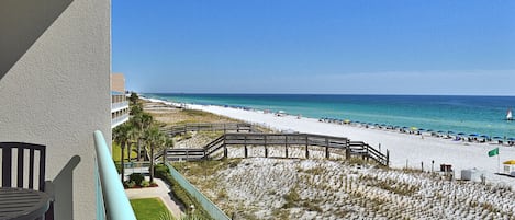 A beach view from a balcony with a wooden deck, sandy beach, and ocean.