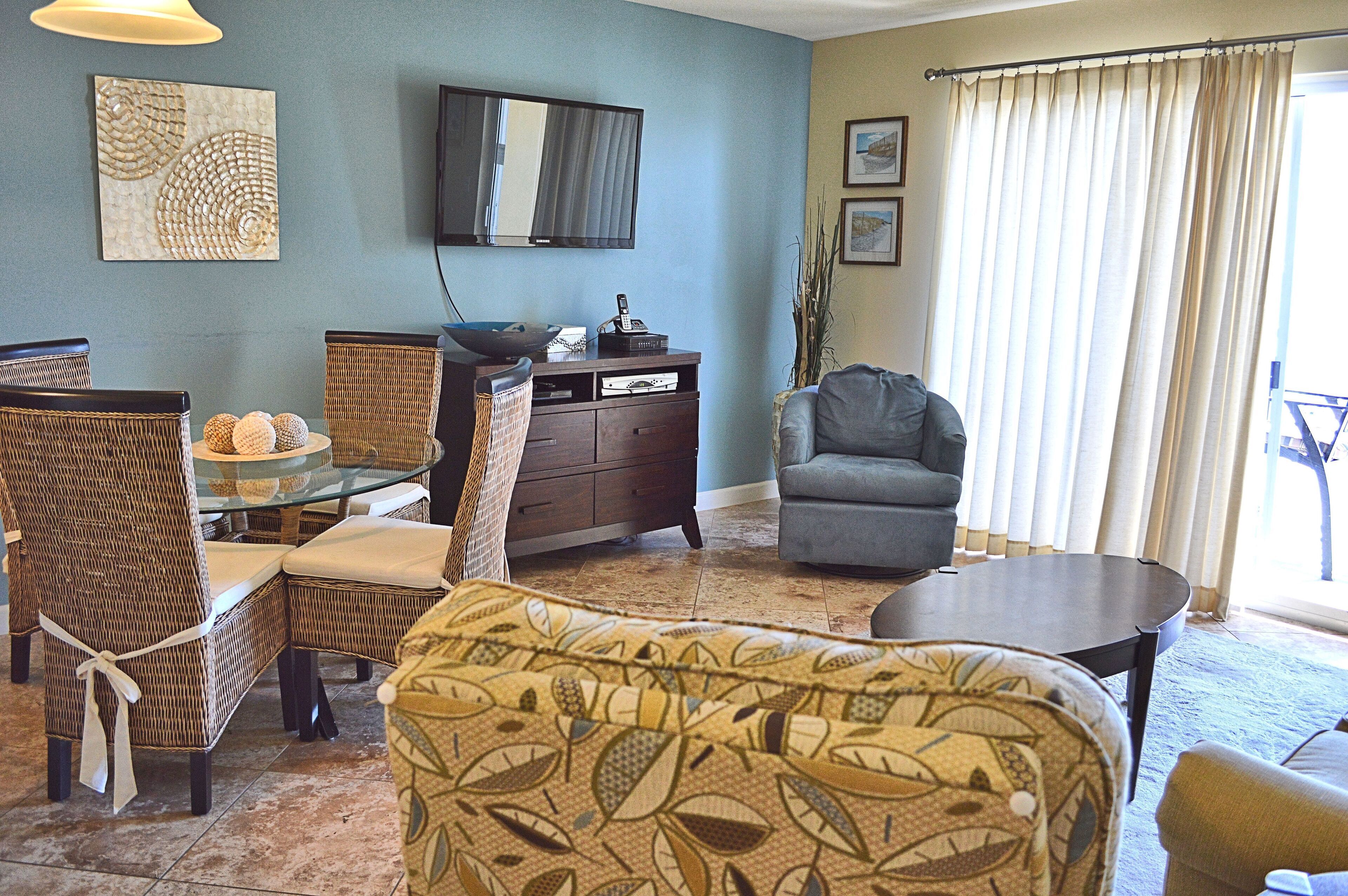 A living room with wicker furniture, a flat-screen TV, and a large window with curtains.