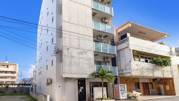 A multi-story building with a balcony on the upper floor, a vending machine, and a small palm tree in front. - Mr.KINJO in Uenokura (Naha)