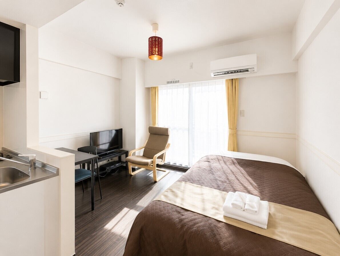 Ein Hotelzimmer mit einem Bett, einem Schreibtisch, einem Stuhl, einem Fernseher und einer Klimaanlage.