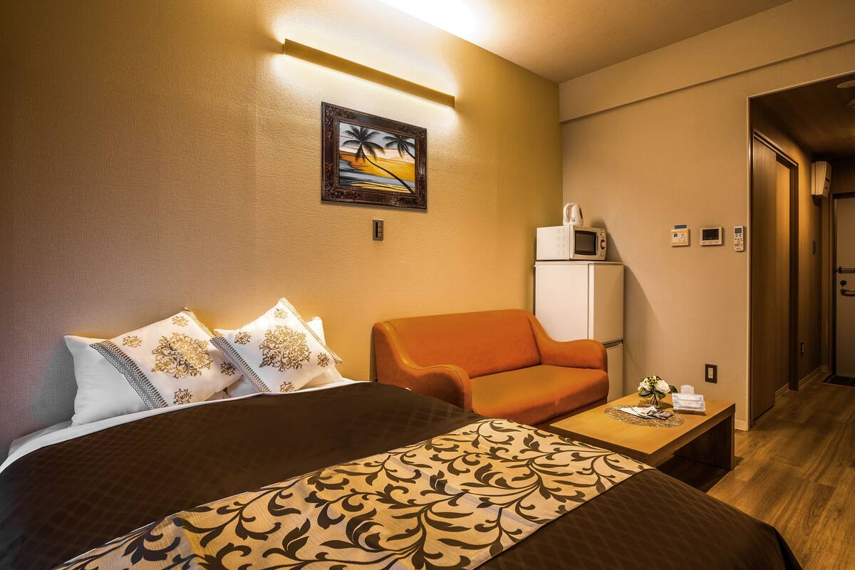 Une chambre d’hôtel avec un lit, un fauteuil orange, une petite table avec un vase et un four à micro-ondes posé sur le comptoir.
