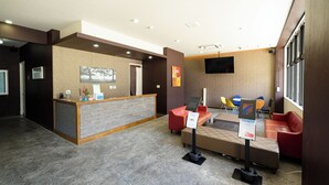 A hotel reception area with a reception desk, seating area, and a mounted television. - Mr. Kinjo inn D-buil (Naha)