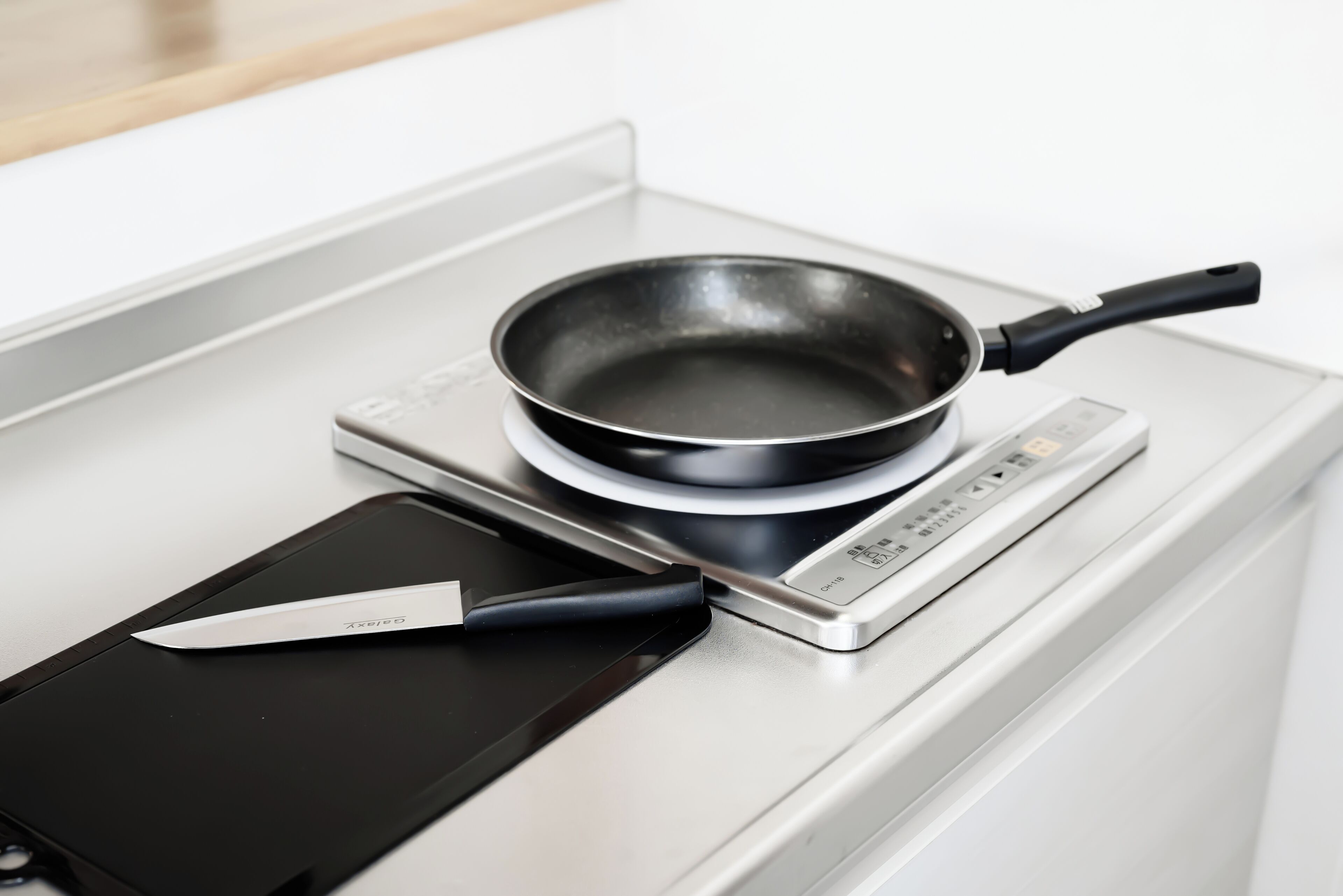Una cocina con estufa, una sartén y un cuchillo sobre una placa de inducción negra.