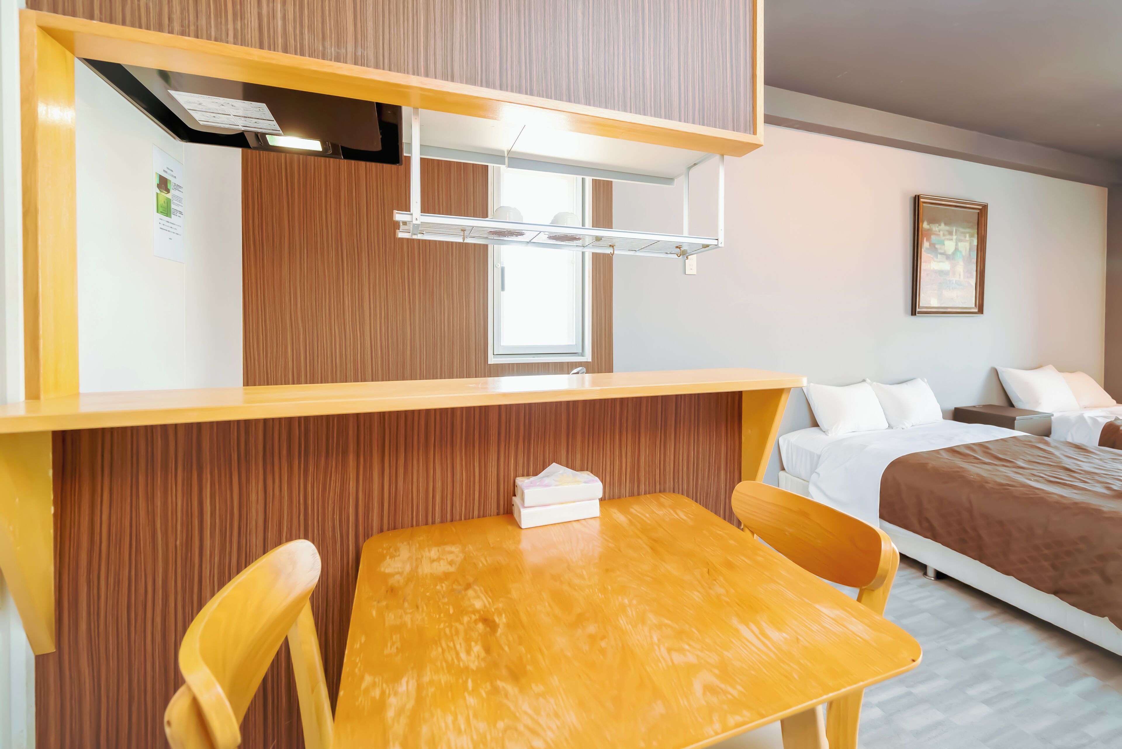 A hotel room with a wooden table and chairs, a bed with white bedding, a wooden partition, and a window.