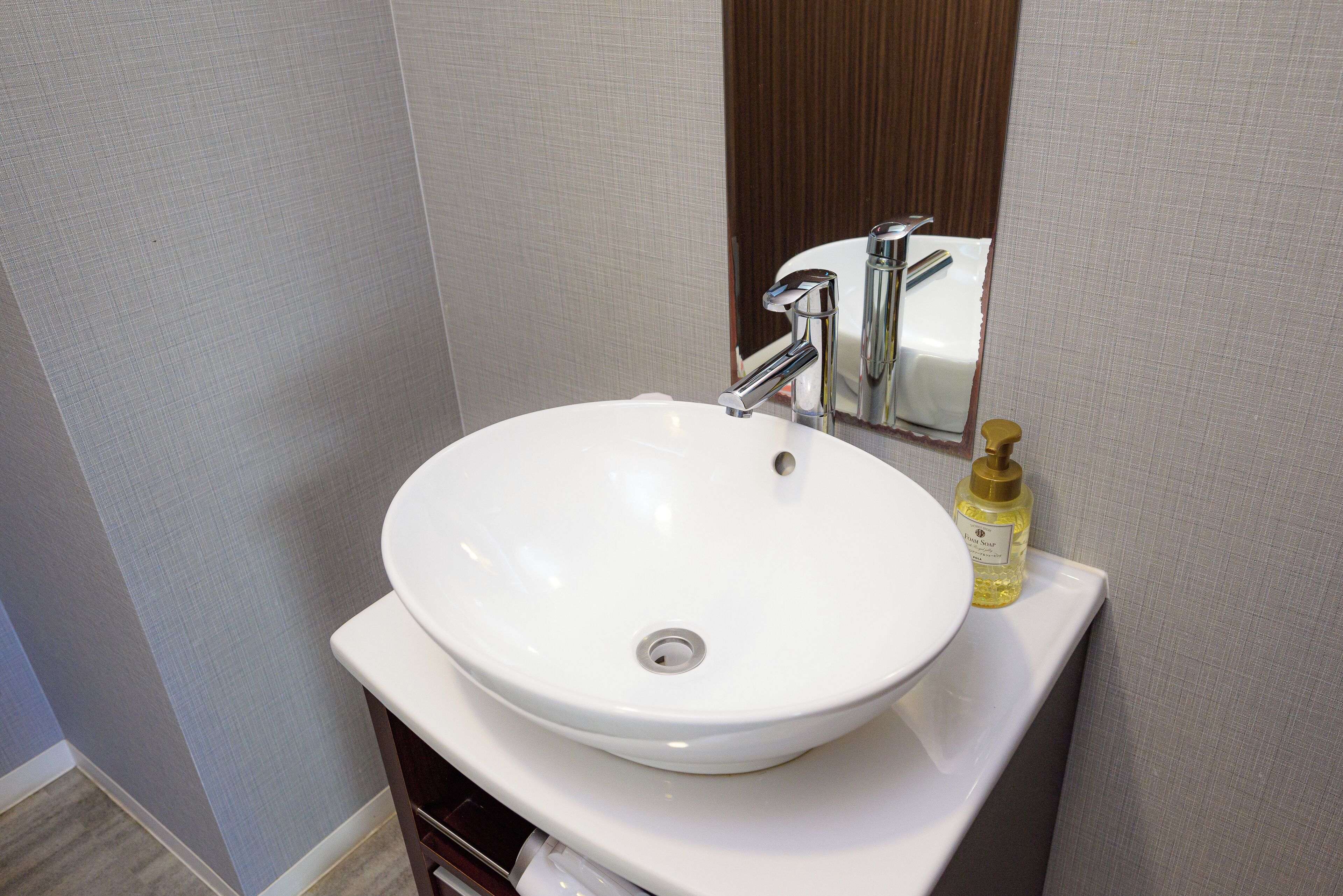 Une salle de bain avec un lavabo blanc, un robinet chromé et un flacon de savon liquide posé sur le comptoir.