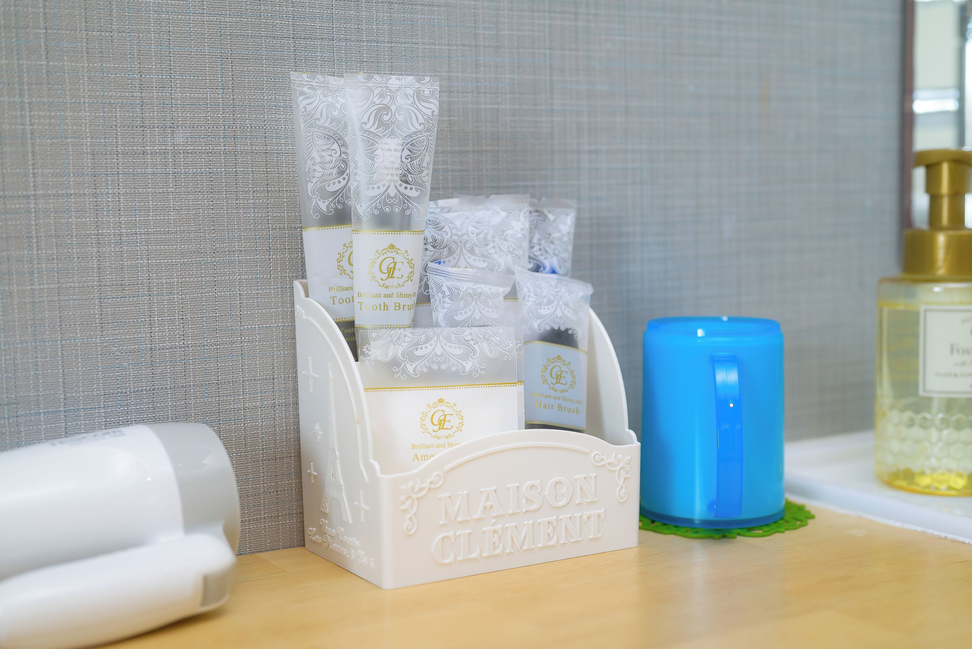 Un organizador de tocador blanco con el nombre de marca "MAISON CLEMENT" y varios artículos de tocador, incluyendo una vela azul y una botella de loción.