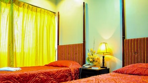 Een hotelkamer met twee bedden, een nachtkastje met een lamp en een raam met gele gordijnen.