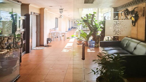 Een hotellobby met een betegelde vloer, een receptiebalie, een bank en verschillende potplanten.