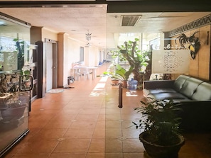 A hotel lobby with a tiled floor, a reception desk, a sofa, and various potted plants. - Ddd Habitat Pension House (Cagayan de Oro)
