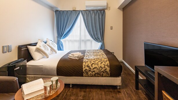 Een hotelkamer met een bed, een televisie, een bureau en een raam met gordijnen.