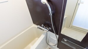 Een moderne badkamer met een witte badkuip, een douche met een handdouche en een glazen plank.