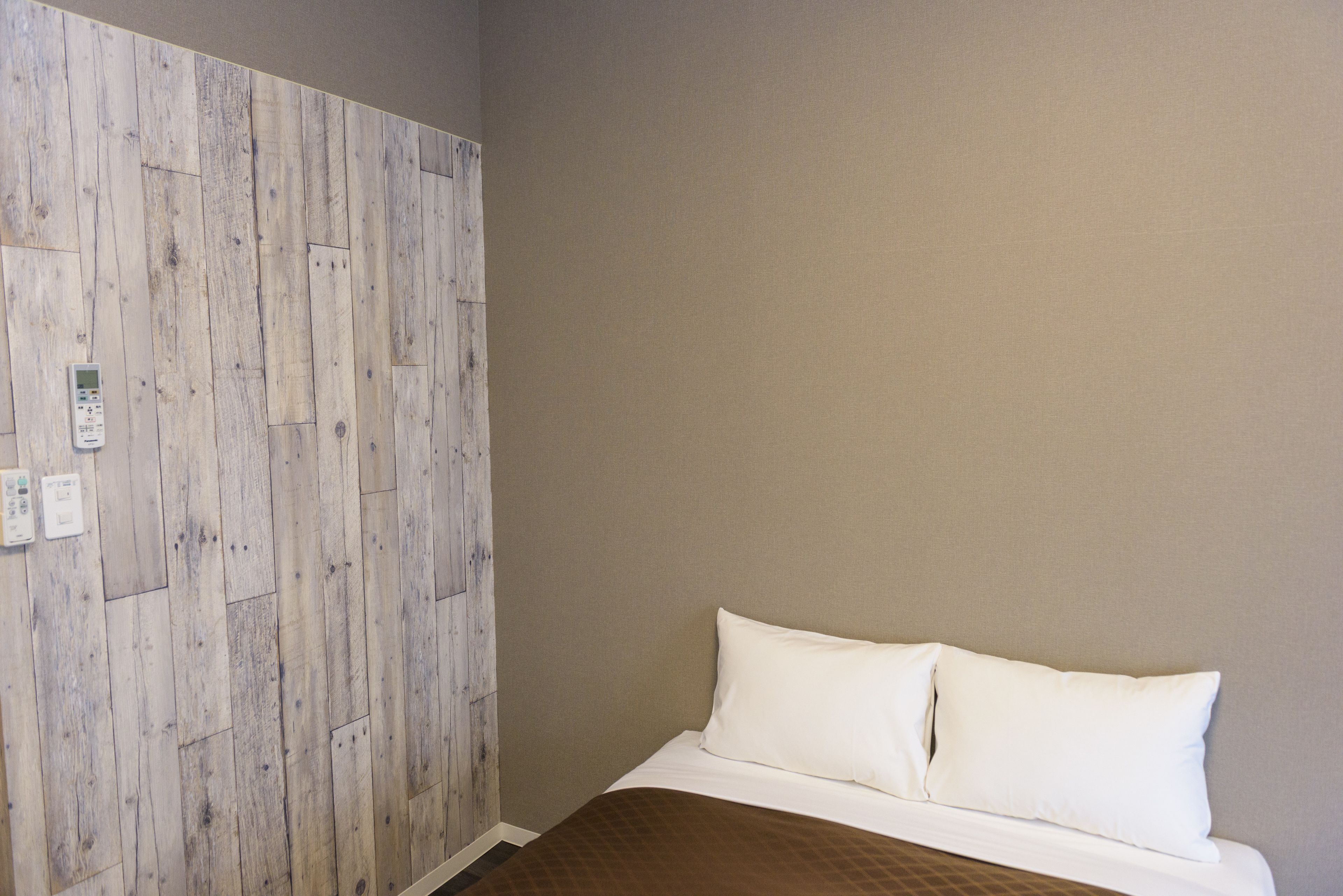 A room with a wooden panel wall, a bed with white bedding, and a control panel on the wall.