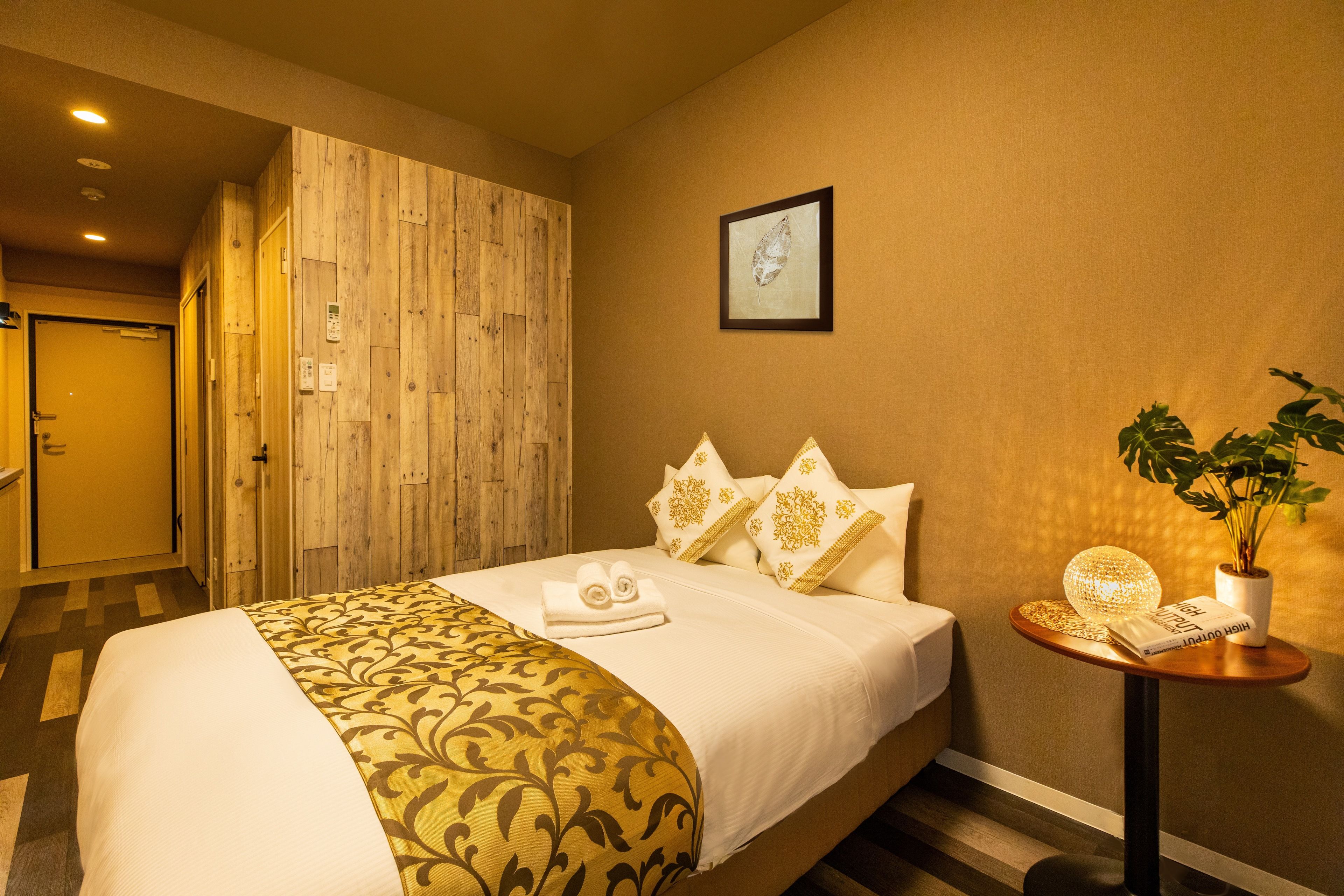 Habitación de hotel con cama, armario de madera, cuadro en la pared y mesita con planta y lámpara.