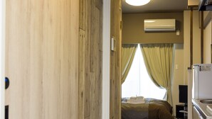Habitación de hotel con un armario de madera, una cama con manta, televisión y una zona de cocina.