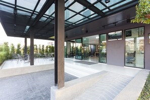 A modern hotel lobby with glass doors, a seating area with tables and chairs, and a view of the cityscape. - Easy Hotel 2 (Lamphun)