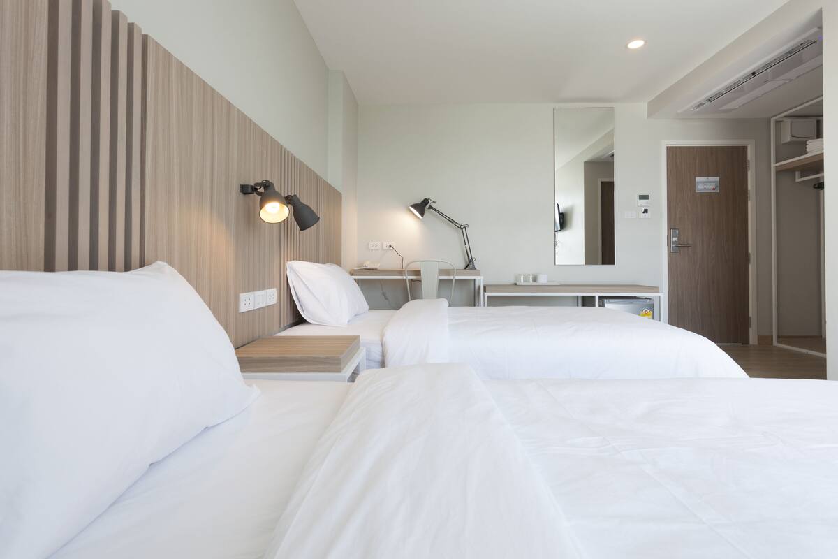 A hotel room with two beds, a wooden headboard, bedside tables with lamps, a mirror, and a wardrobe.