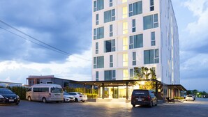 Un hotel moderno con una estructura de varios pisos, un acceso cubierto y un estacionamiento con varios vehículos.