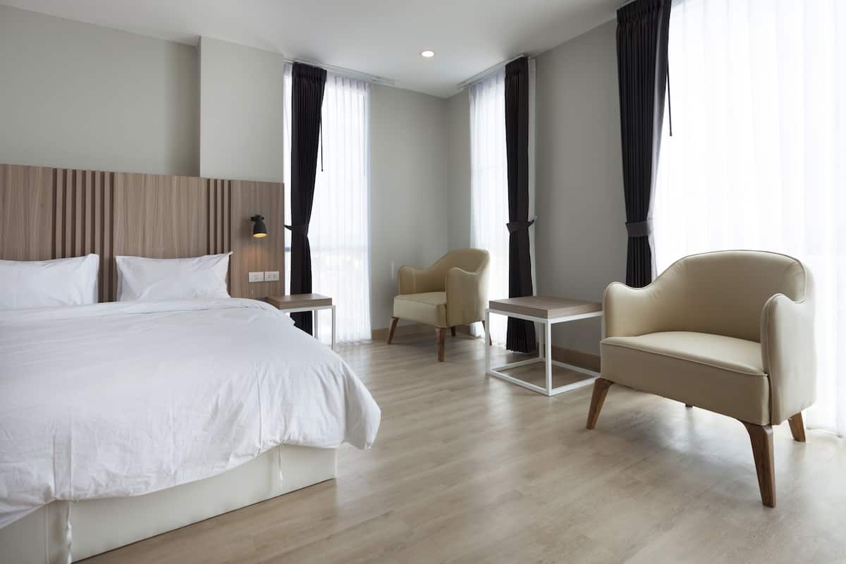 A modern hotel room with a large bed, two armchairs, a small table, and a nightstand.