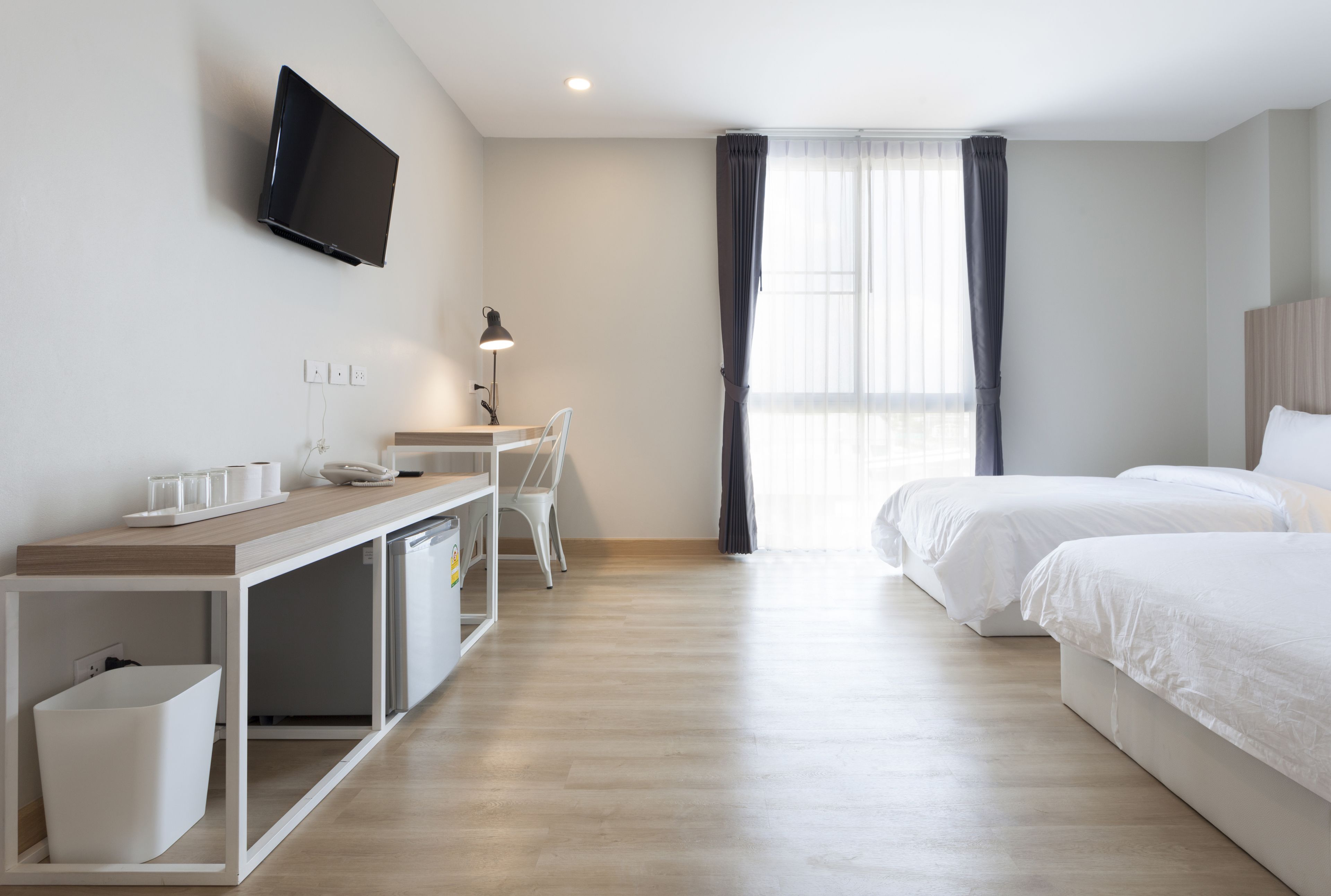Una habitación de hotel con escritorio, silla, dos camas, televisor y ventana con cortinas.