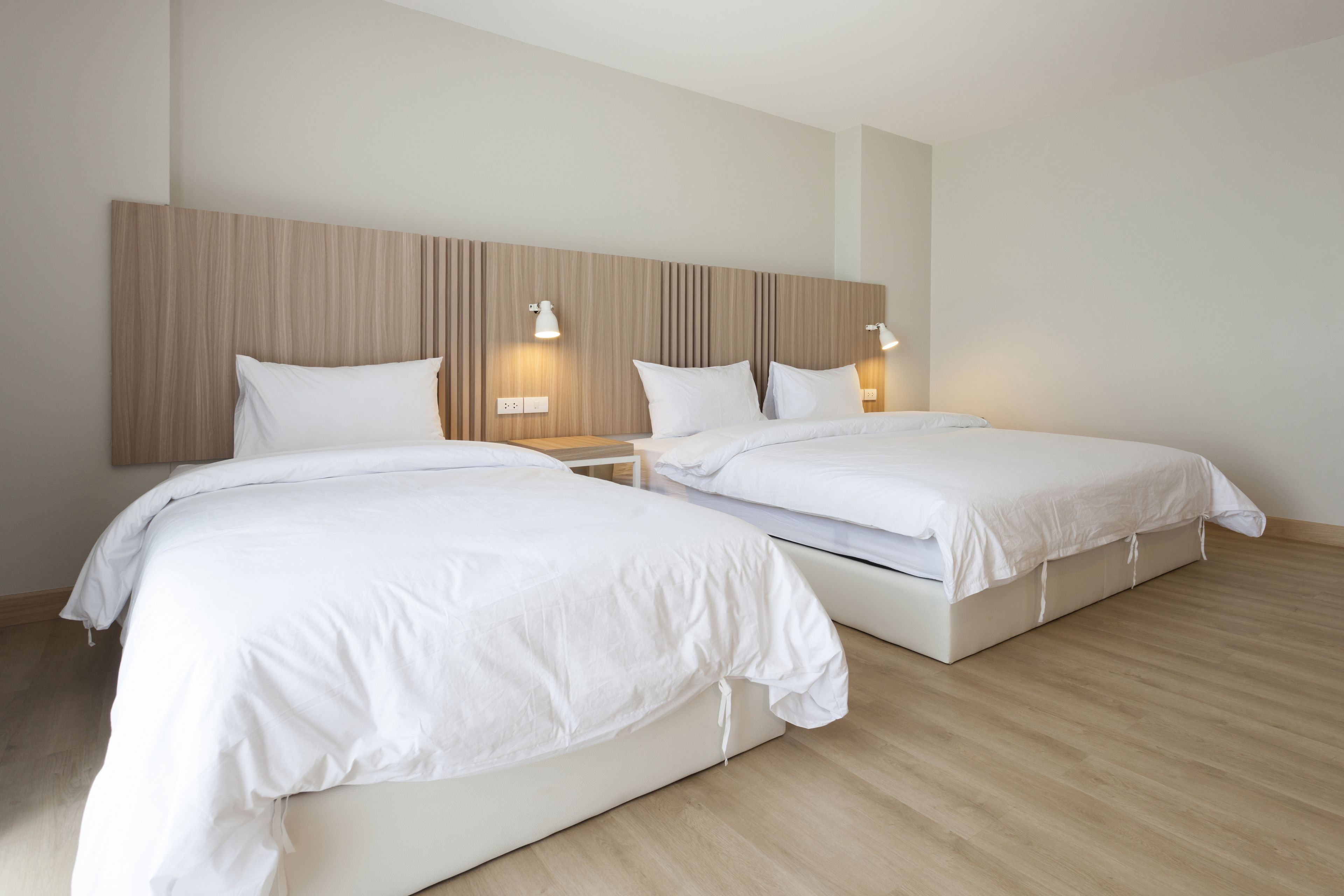 Una habitación de hotel moderna con dos camas individuales, cabecero de madera, lámparas de noche y suelo de madera.
