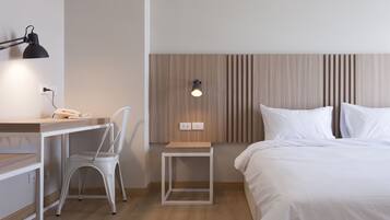 Quarto de hotel com cama, escrivaninha com cadeira, mesa pequena, abajur e luminária na parede.
