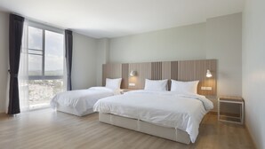 Habitación de hotel con dos camas, un ventanal con cortinas, cabecero de madera, lámparas de noche y vistas a la ciudad.