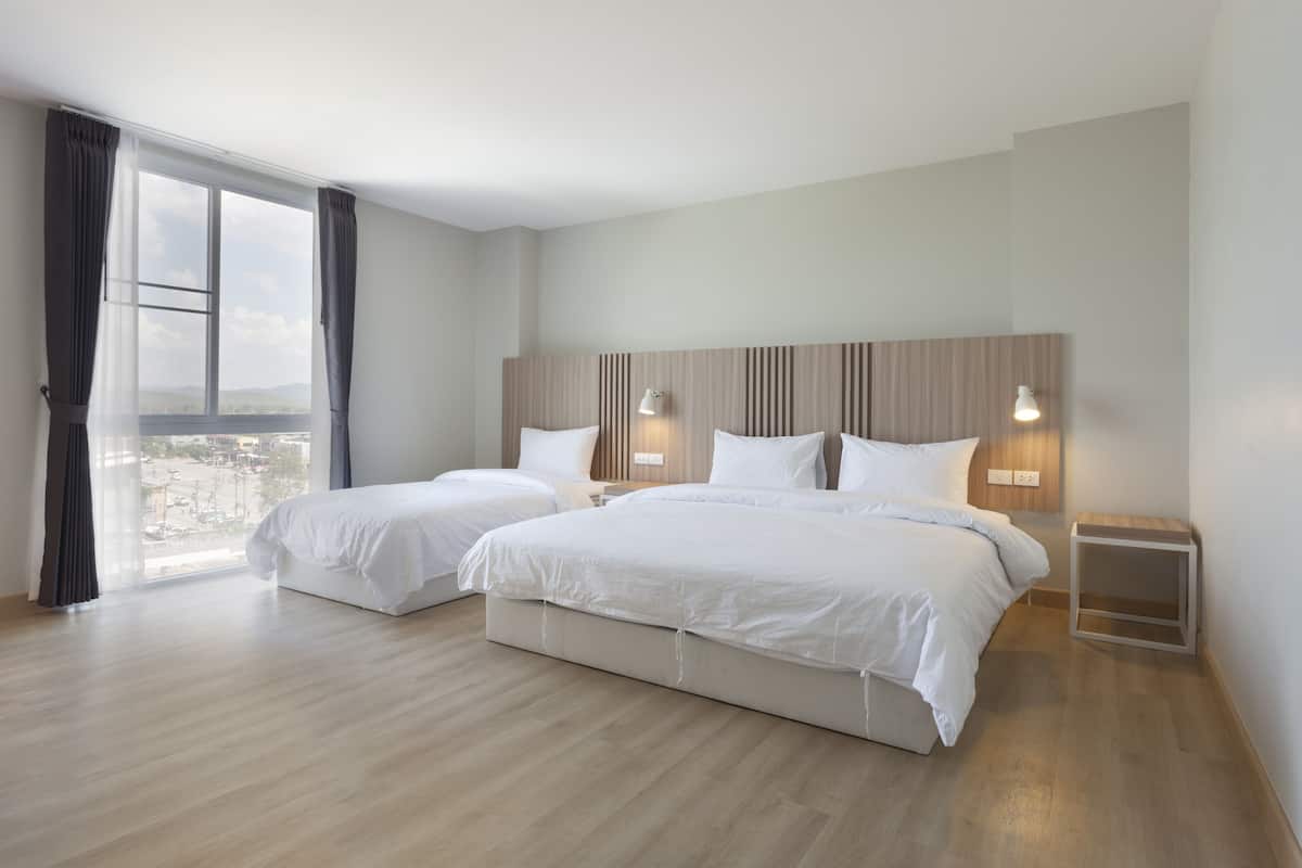 A hotel room with two beds, a large window with curtains, a wooden headboard, bedside lamps, and a view of the city.