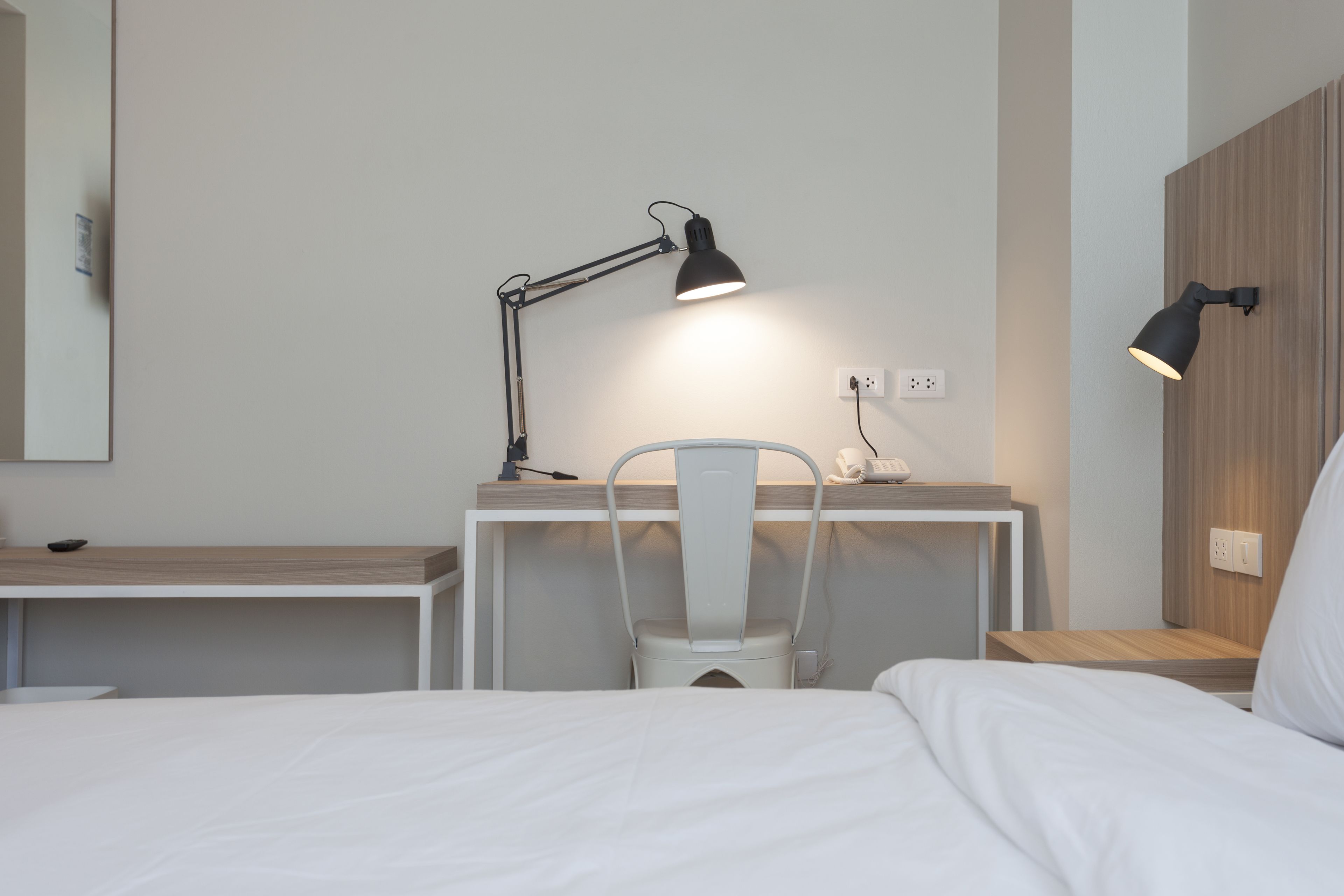 A hotel room with a bed, a desk with a chair, and two bedside lamps.