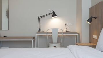 A hotel room with a bed, a desk with a chair, and two bedside lamps.