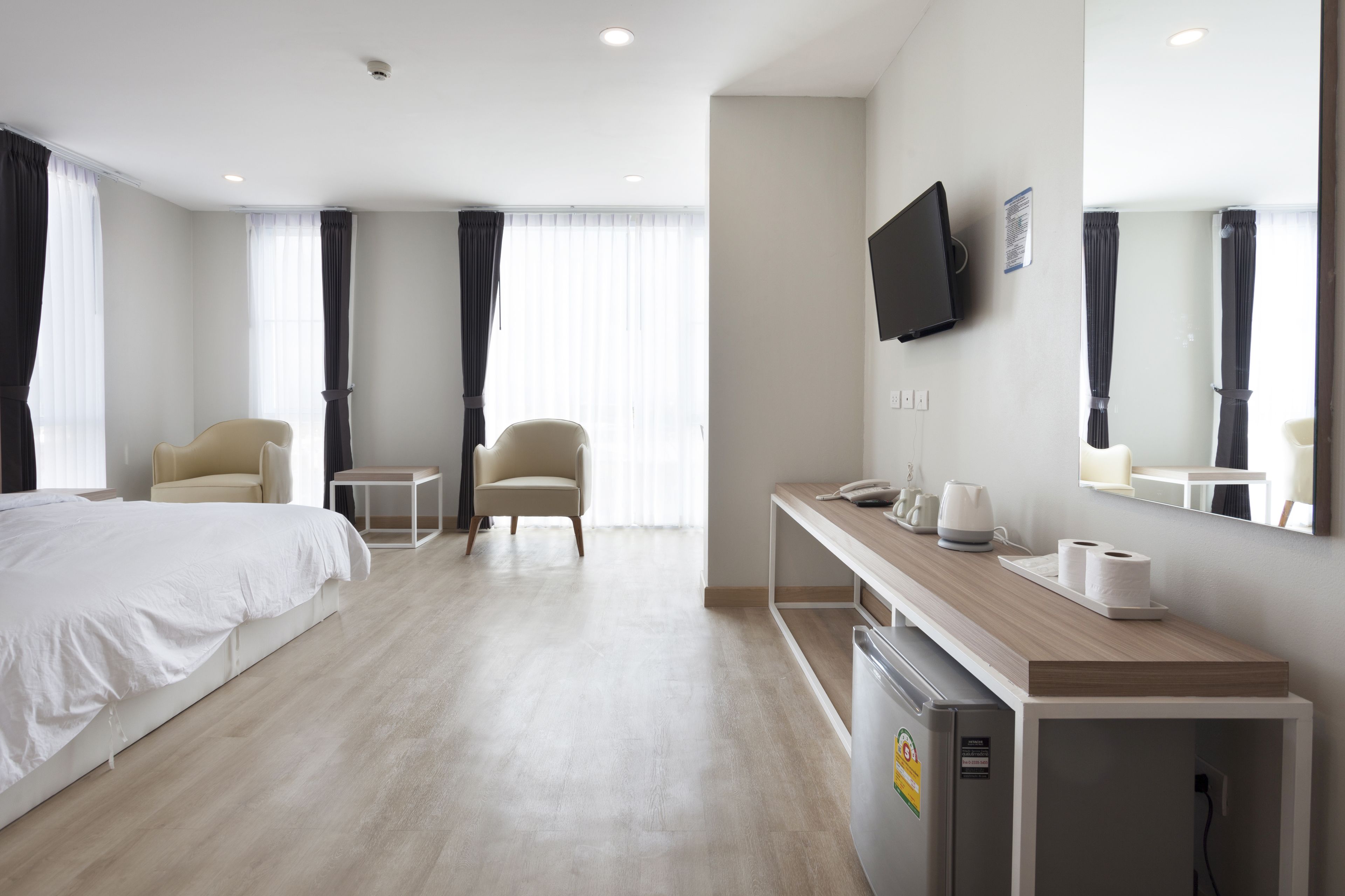 Hotelkamer met een bed, twee stoelen, een bureau met spiegel, een televisie en een kleine koelkast.
