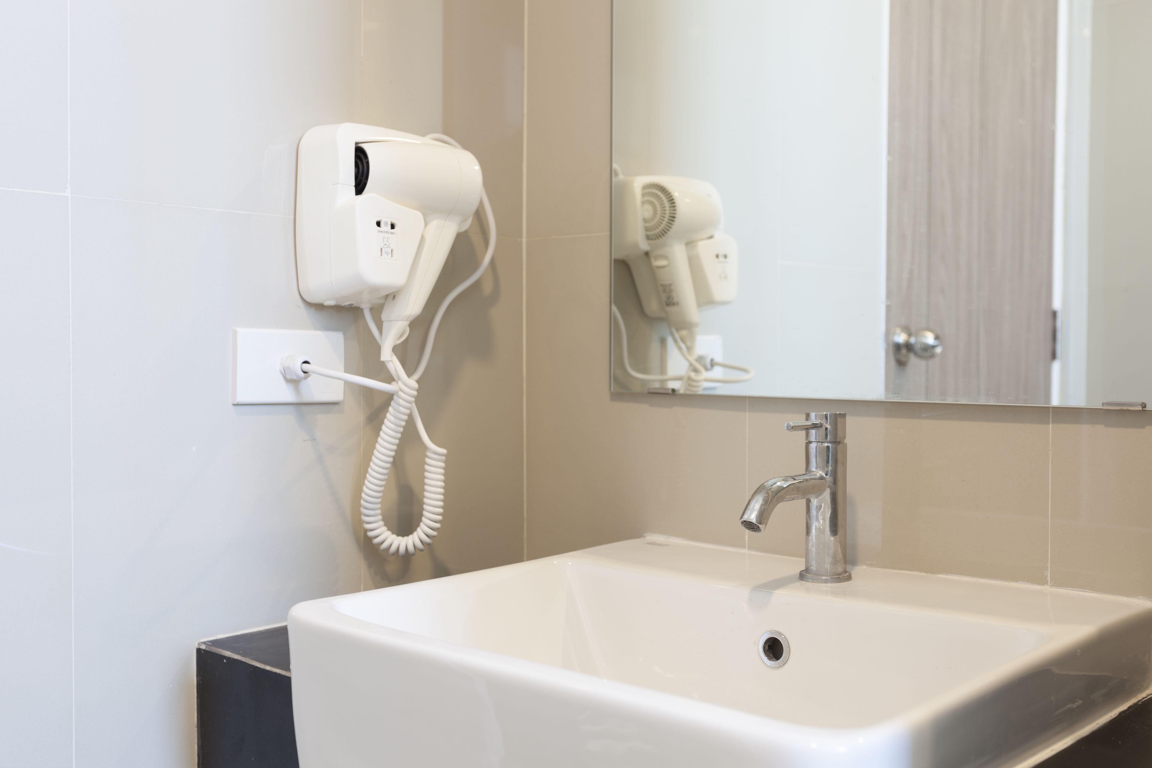 Un bagno con un lavandino bianco, uno specchio e due asciugacapelli montati a parete.