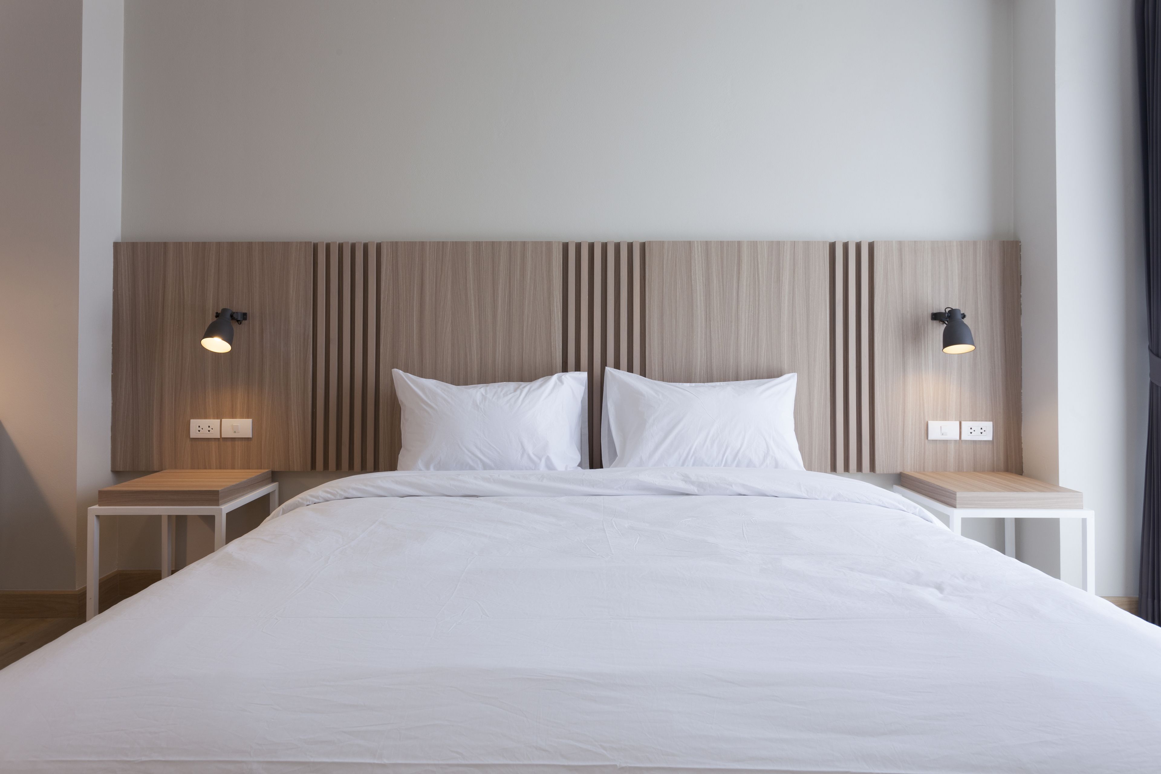 A modern hotel room with a large bed, two bedside tables, and a wooden headboard.