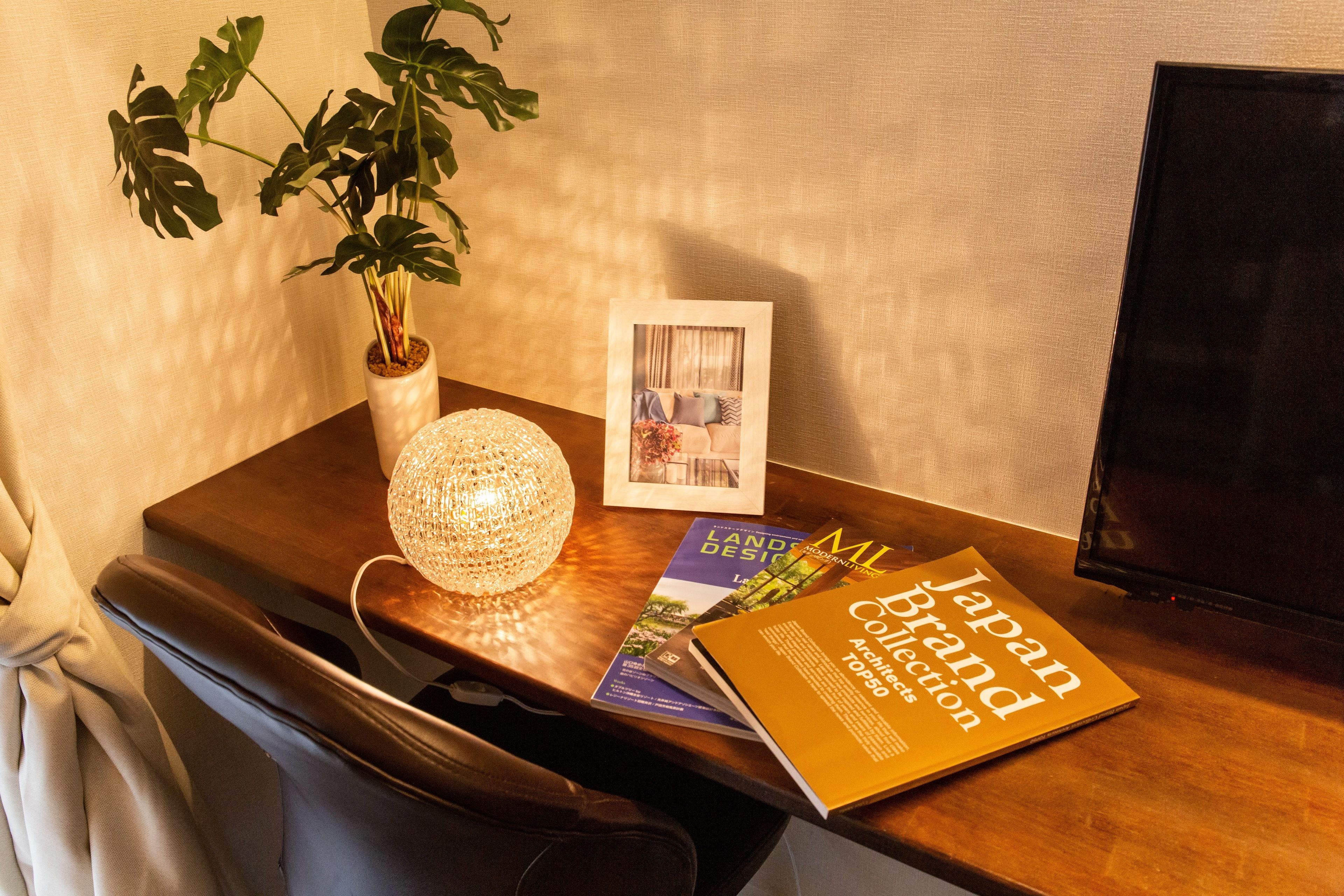 Un escritorio de madera con una planta en maceta, una foto enmarcada, una lámpara y un libro titulado 'Japan Brand Collection'.