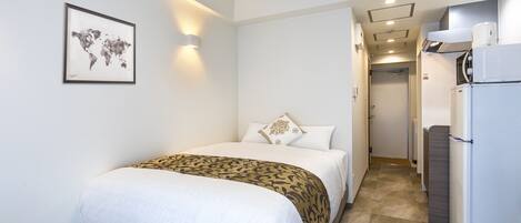 Habitación de hotel con cama, un mapa mundial en la pared, refrigerador y un pasillo que lleva a una puerta.