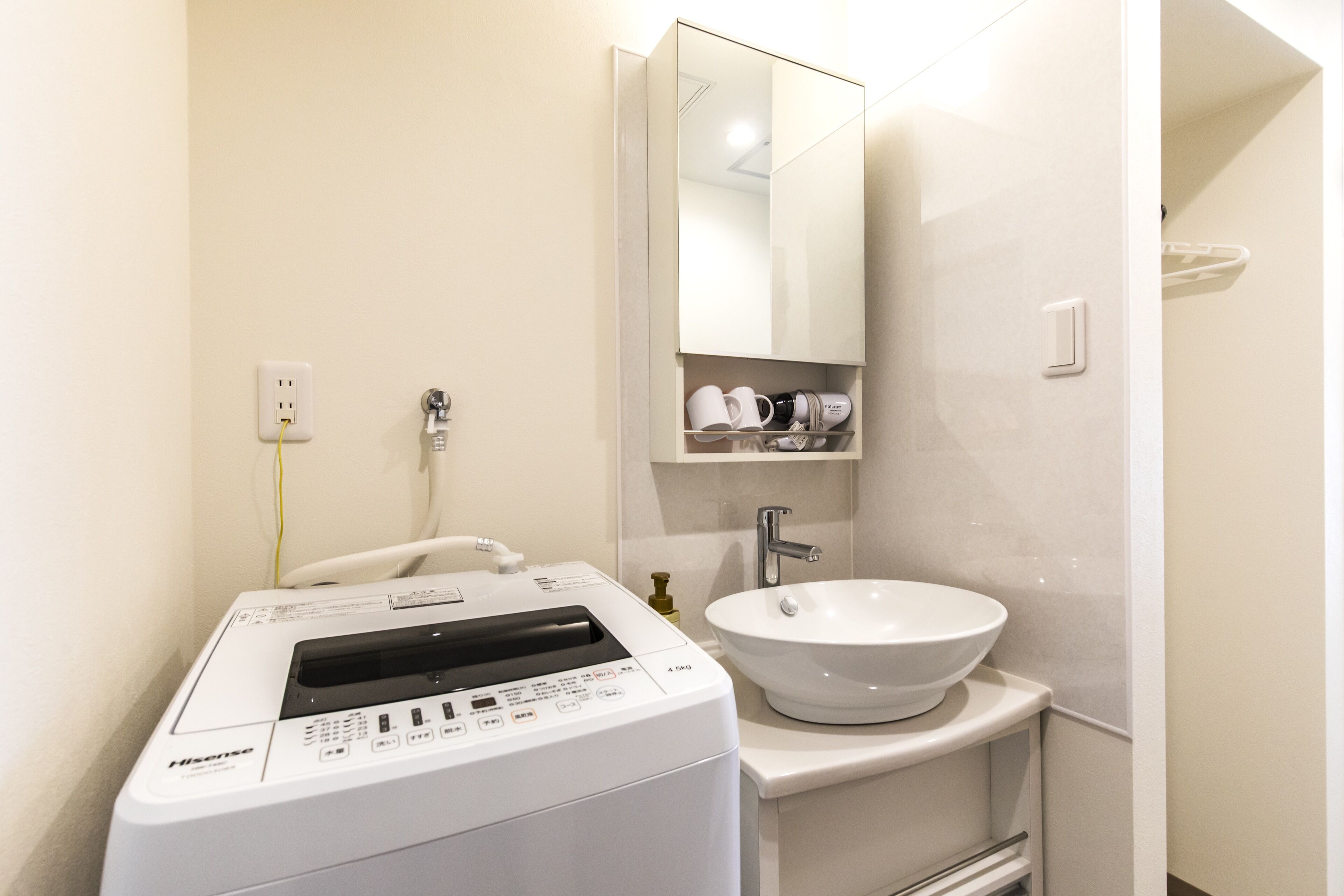 A compact bathroom with a front-loading washing machine, a sink, and a mirror above it.