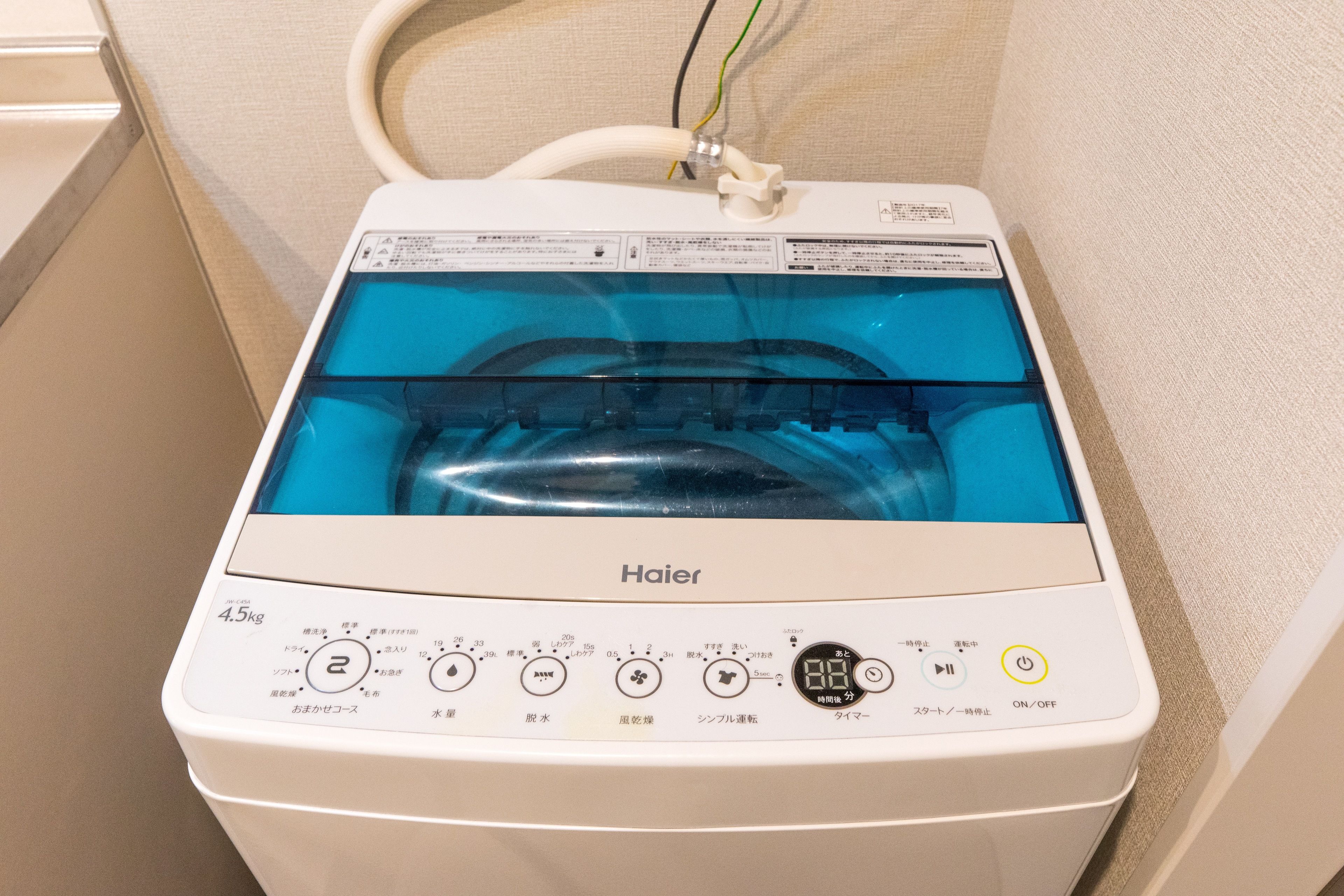 A Haier washing machine with a transparent water tank, control panel with various settings, and a power cord plugged in.