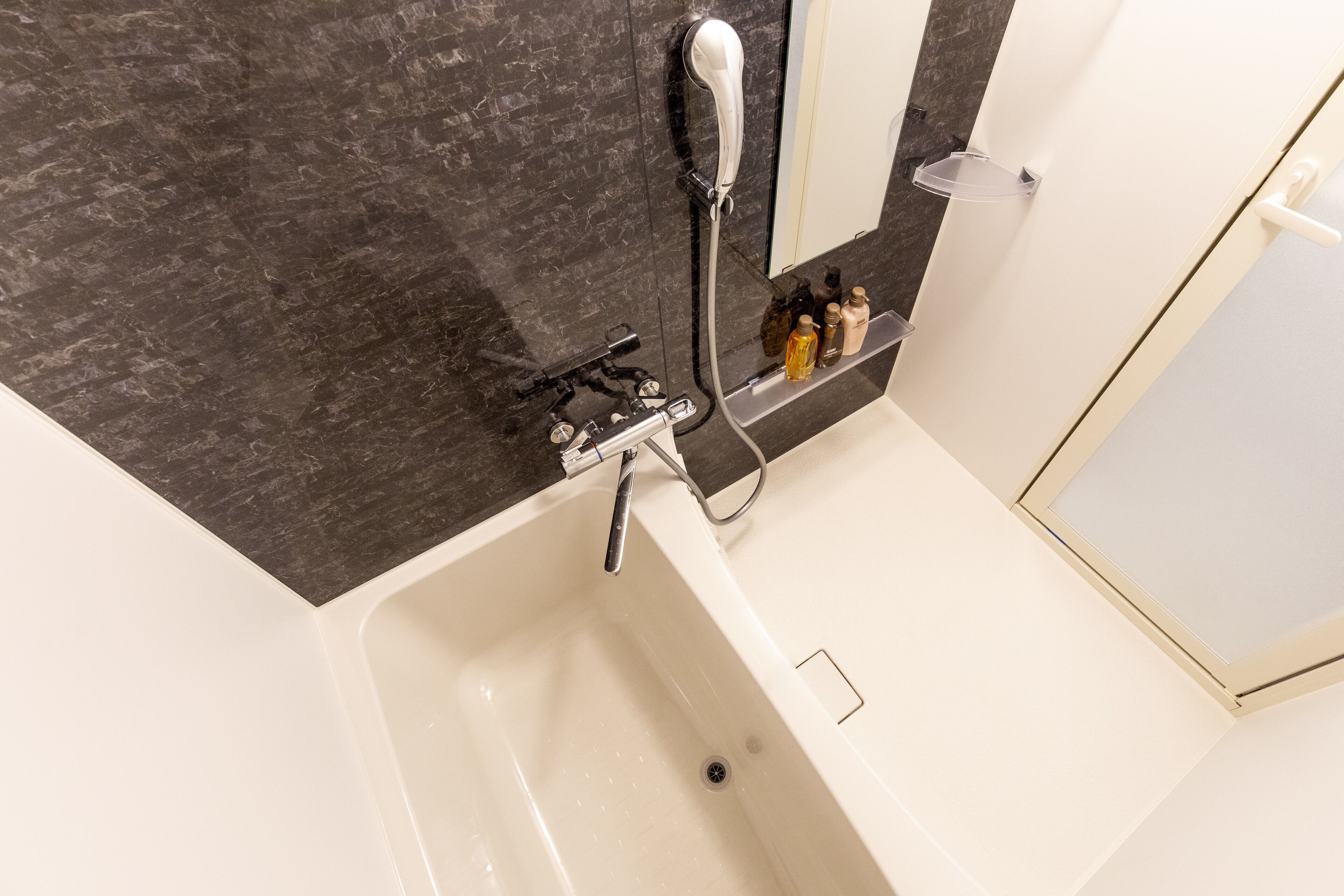 Une salle de bain moderne avec une baignoire blanche, un mur en marbre foncé et une pomme de douche.