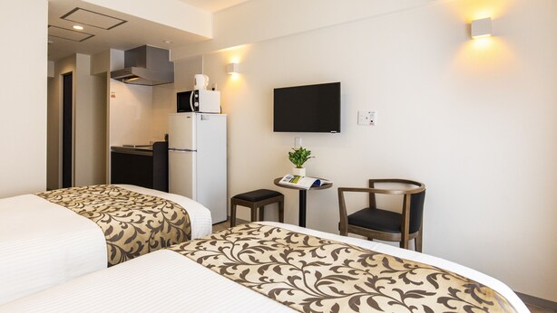 Ett hotellrum med två sängar, ett skrivbord, en stol, en tv och ett litet bord med en växt.