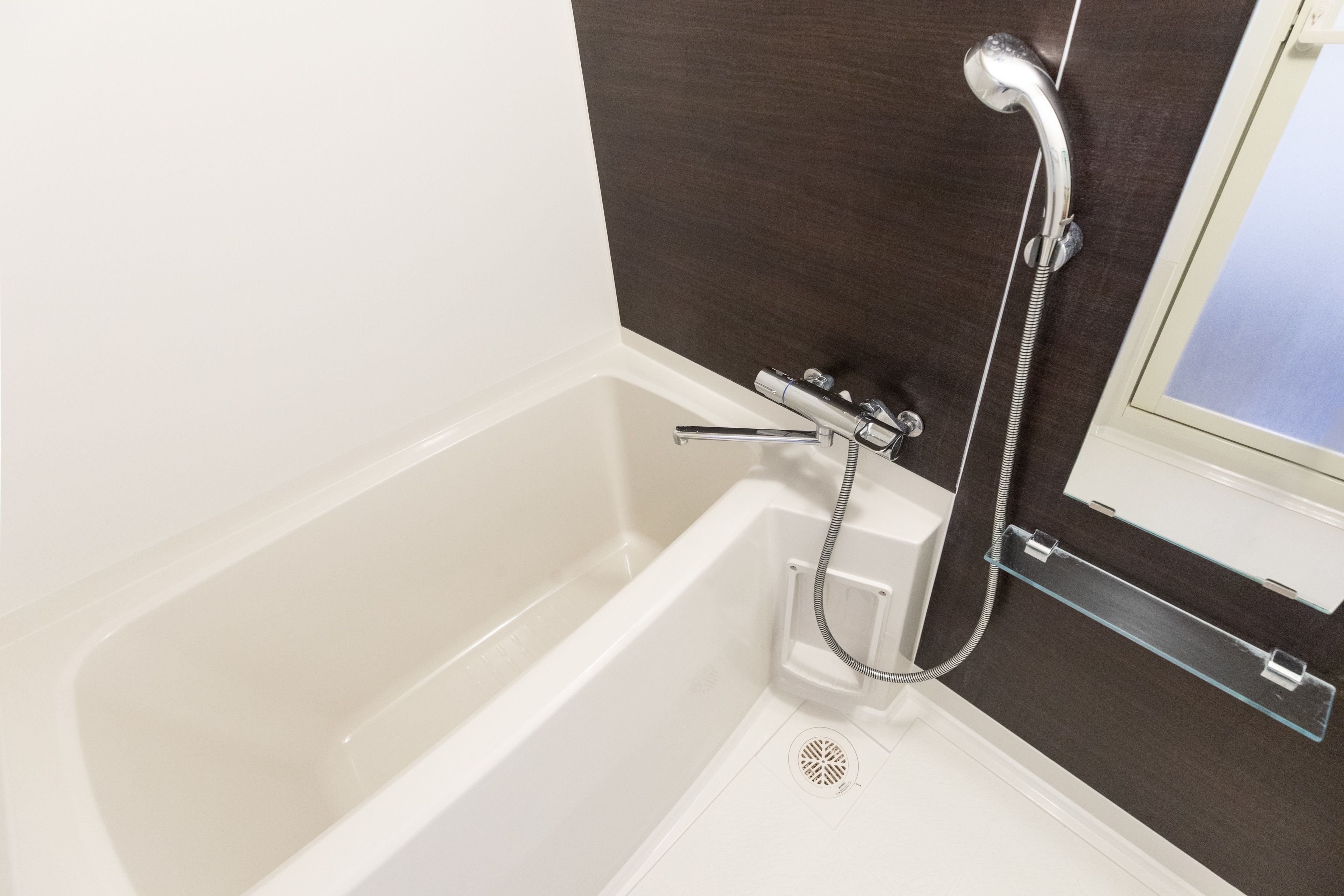 Un baño moderno con una bañera blanca, una ducha con cabezal de mano y un estante de vidrio.