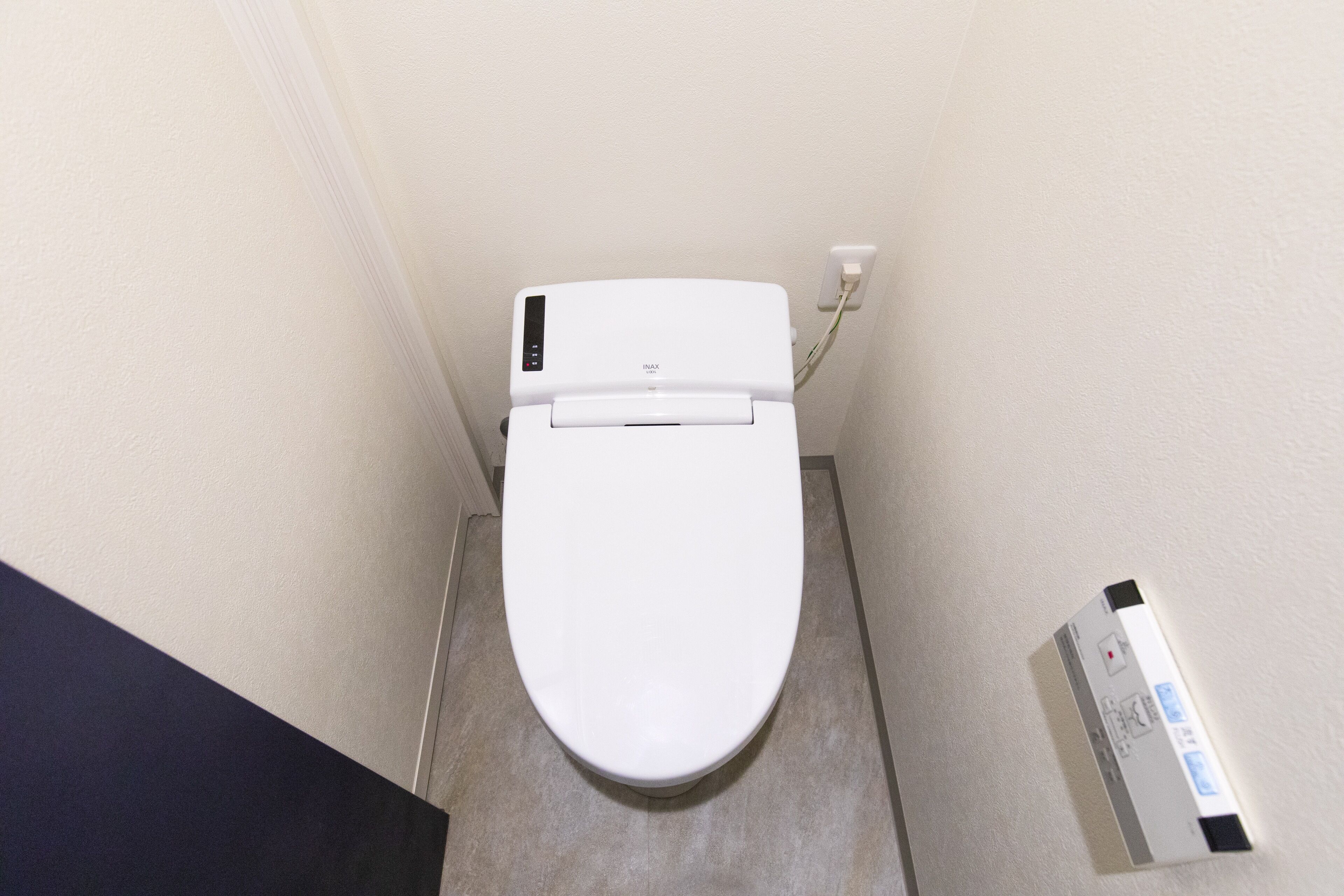 Inodoro blanco con panel de control y dispositivo fijado a la pared a la derecha.
