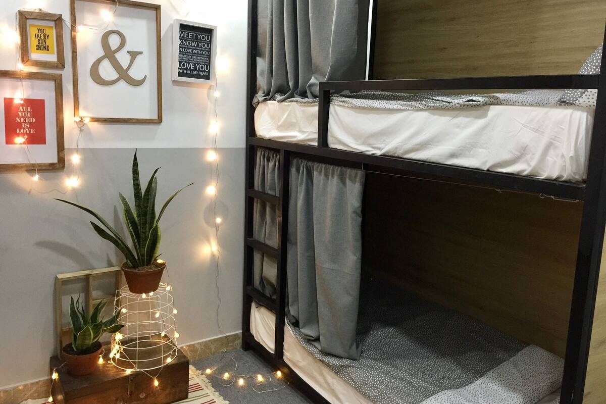 Un lit superposé avec une structure en bois et une literie blanche, une plante en pot, des guirlandes lumineuses et des affiches motivantes accrochées au mur.