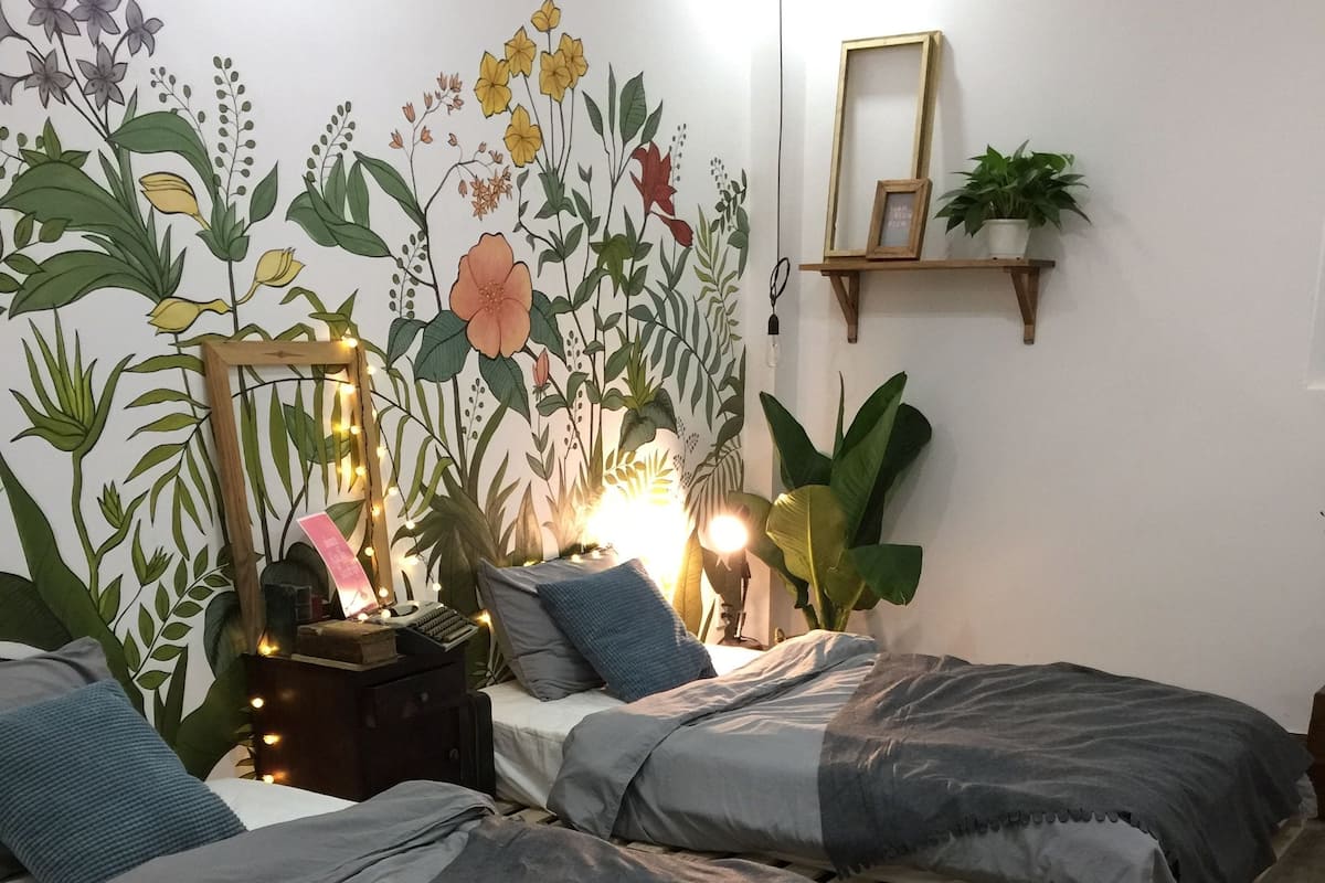 Une chambre avec deux lits, une table de chevet, une lampe et une fresque murale.