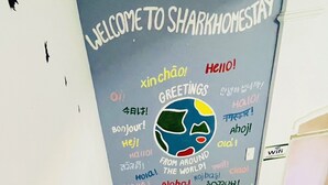A staircase with a wall featuring a 'Welcome to Sharkhomestay' sign and a colorful world map surrounded by various greetings in multiple languages. - Shark Hotel - Hostel (Hue)