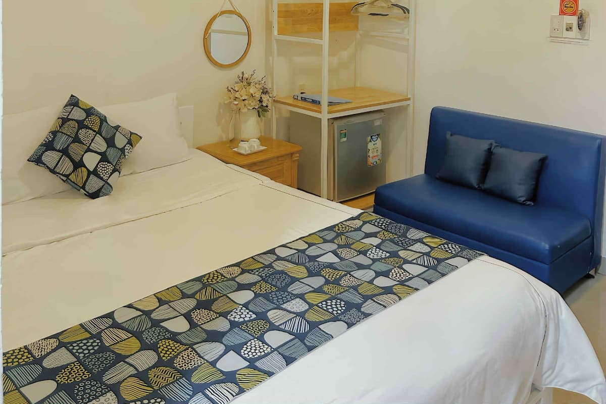 A hotel room with a bed, a blue sofa, a wardrobe, a small desk, and a mirror on the wall.
