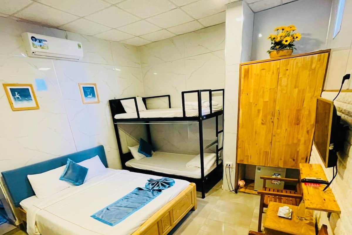 A hotel room with a large bed, a smaller bunk bed, a wooden desk, and a wooden wardrobe.